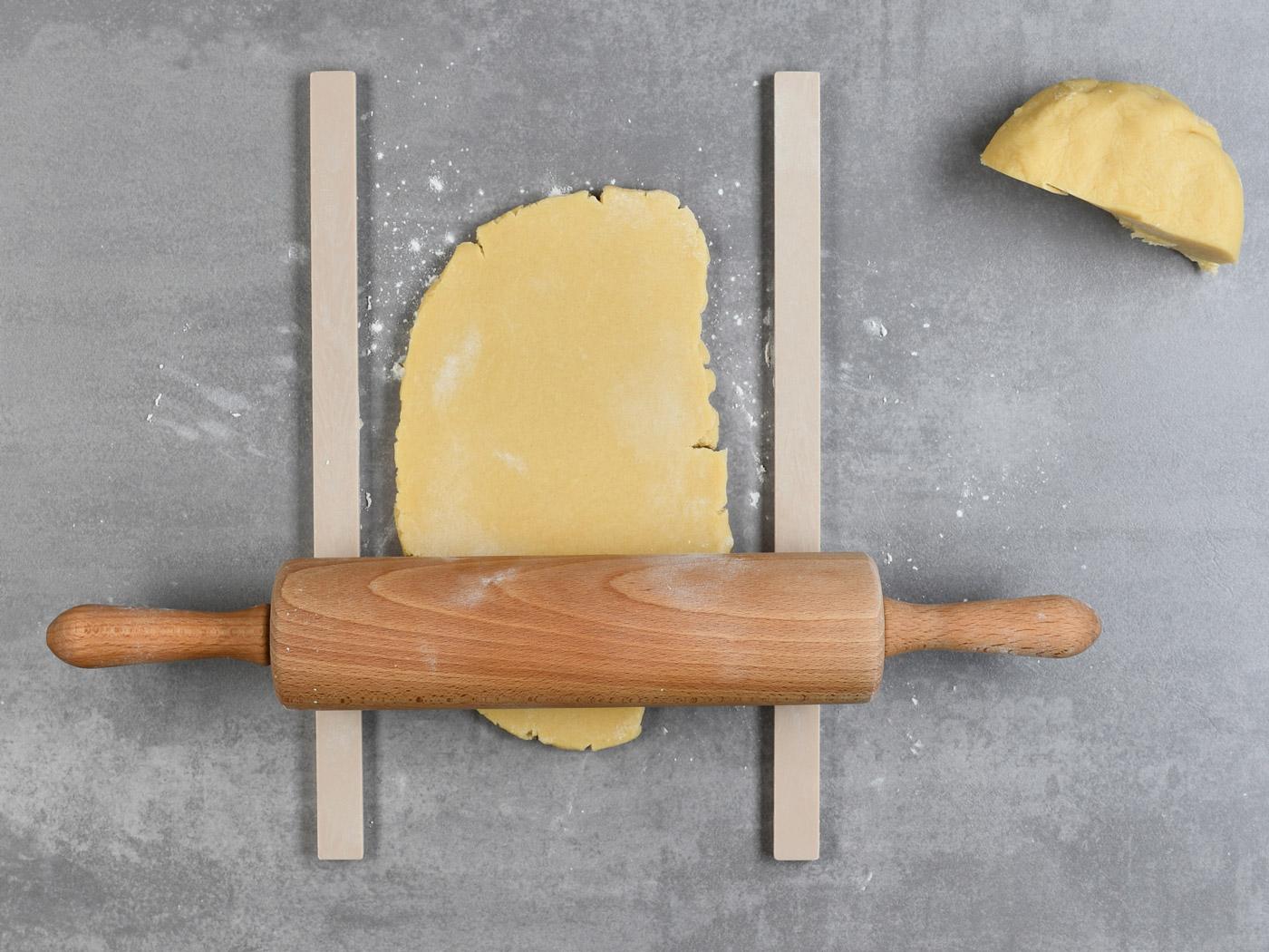 Wallholz liegt auf ausgerolltem Teig zwischen zwei Holzleisten.