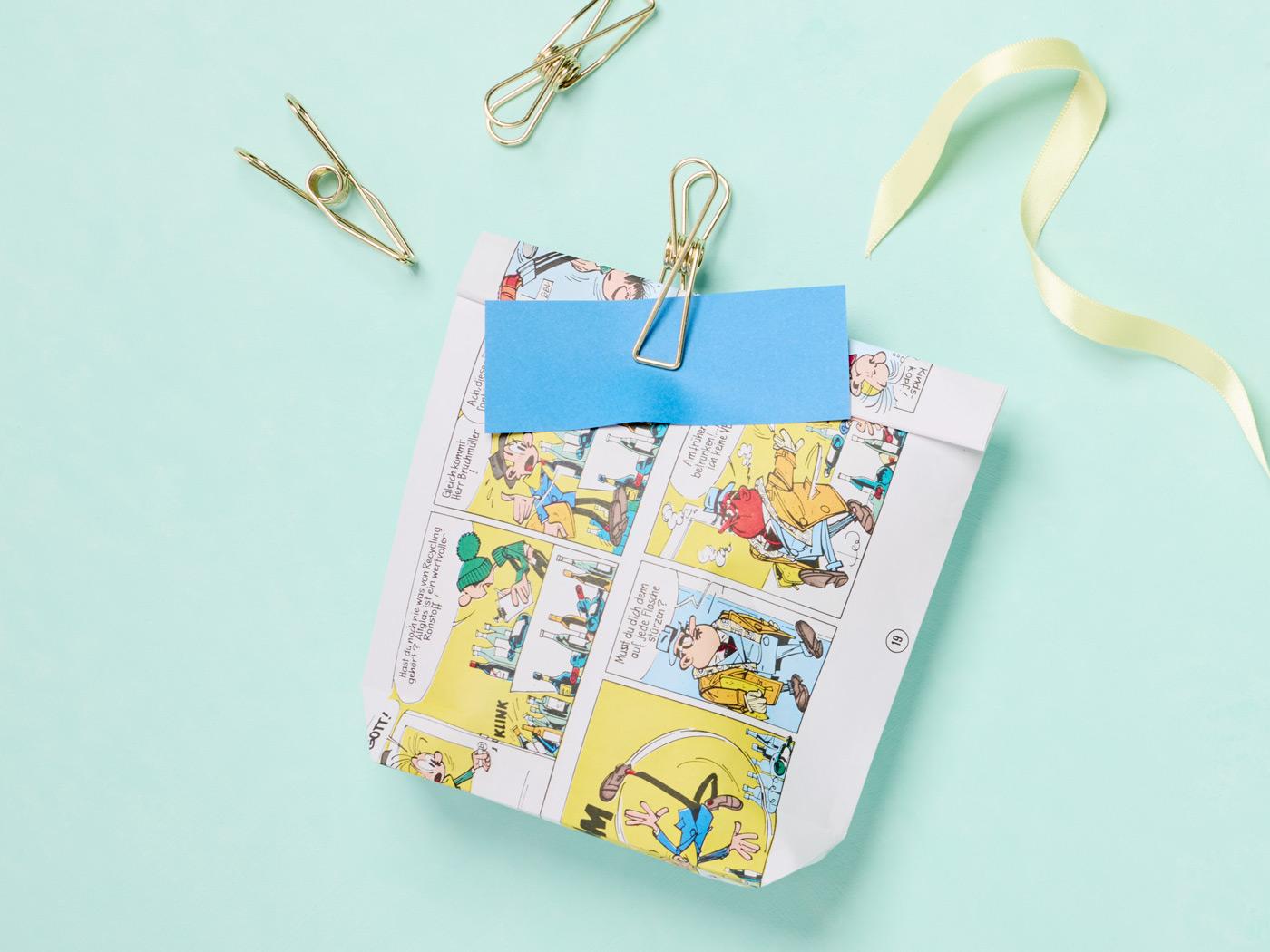 Kleine Papiertüte aus buntem Comicpapier mit Klammern und blauem Zettel verschlossen.