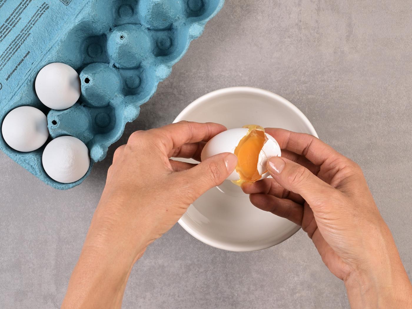 Hände halten ein aufgeschlagenes Ei mit orangefarbenem Eigelb.