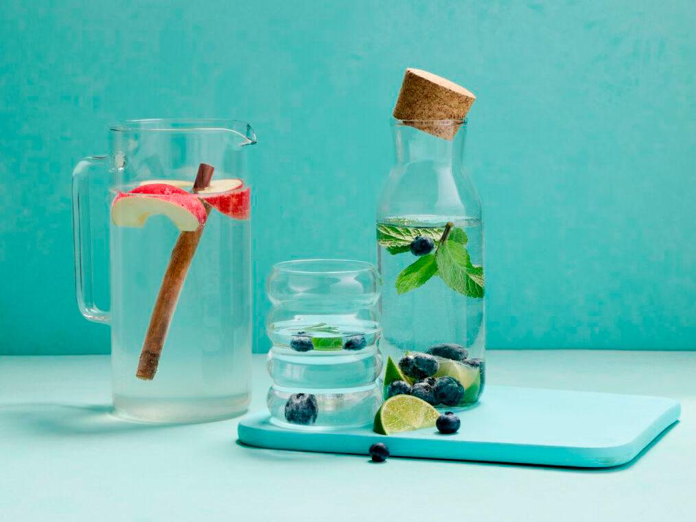 Zwei Wasserkrüge mit Apfel, Limette, Heidelbeeren und Minze auf einem hellblauen Brett.
