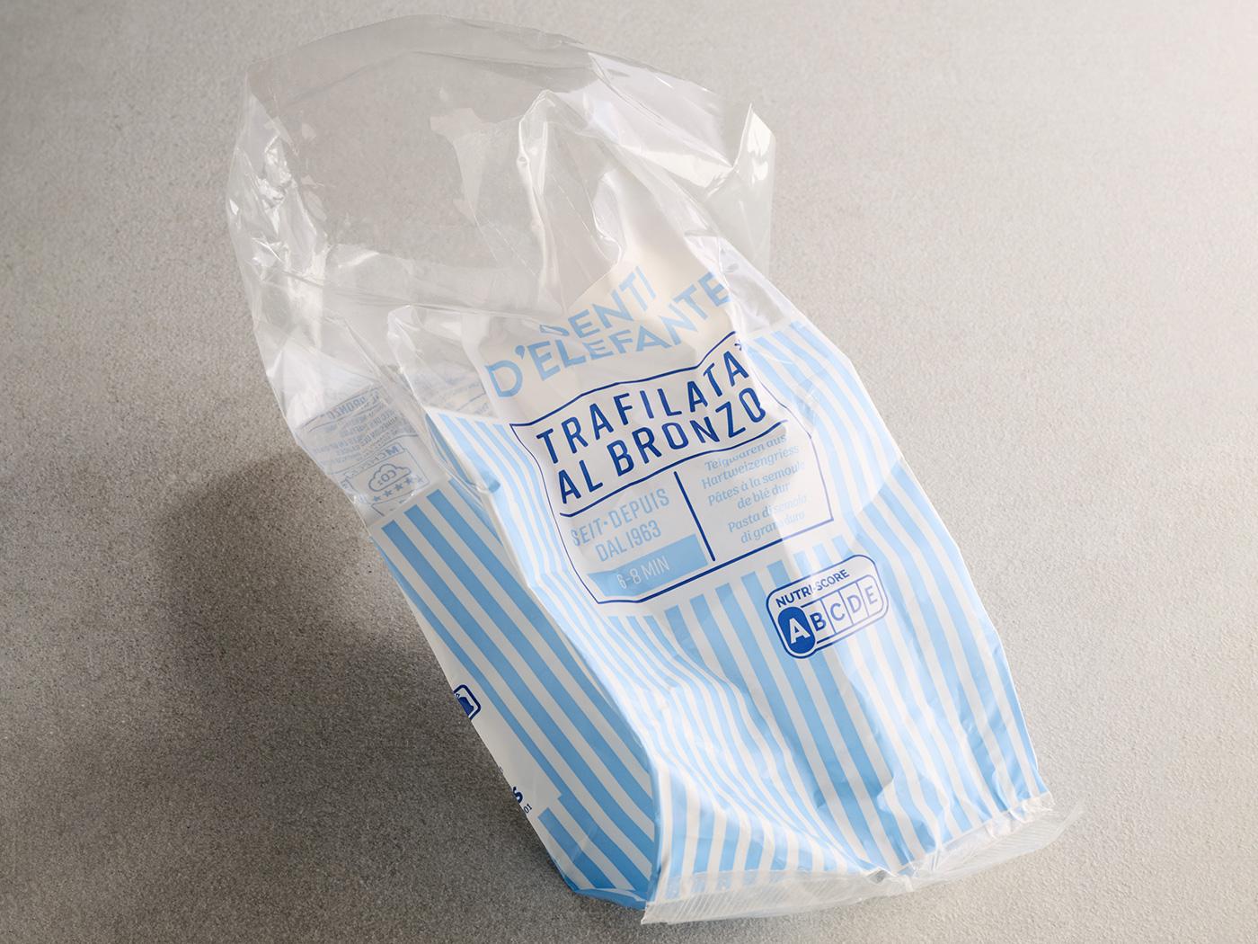 Leere, blau-weiss gestreifte Pasta­verpackung aus Plastik liegt auf grauem Untergrund.