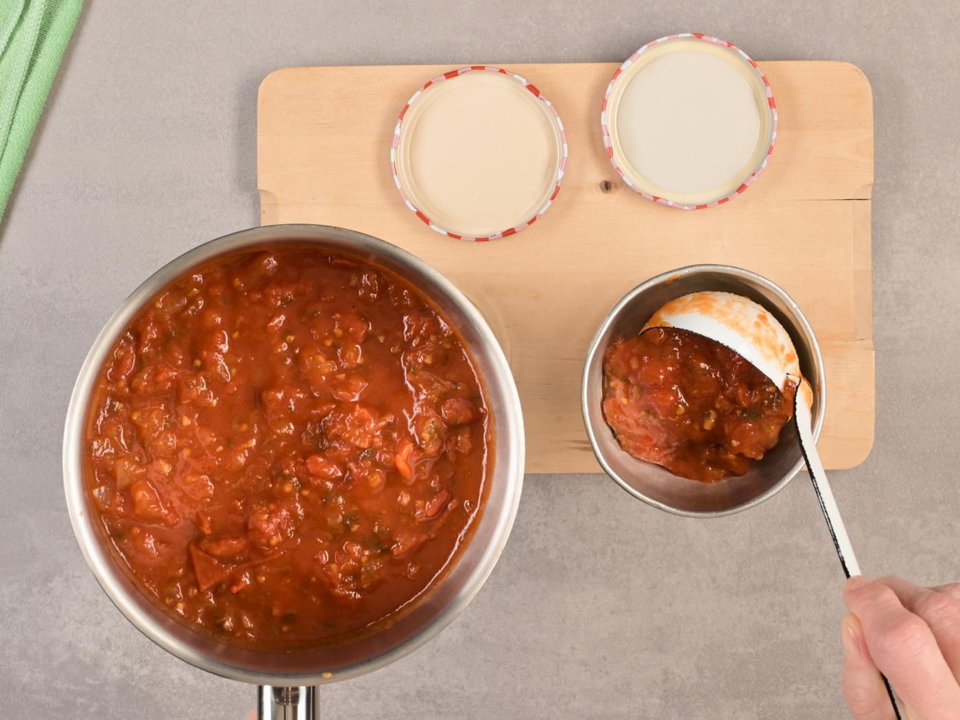 Tomatensauce wird mit Kelle in Glas gefüllt.