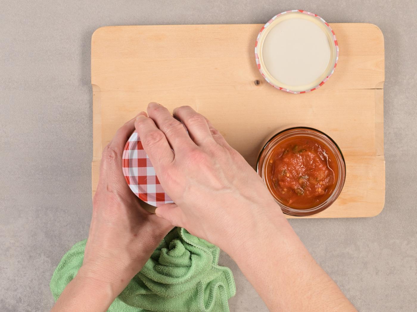 Hände verschliessen ein geöffnetes Glas mit Tomatensauce.