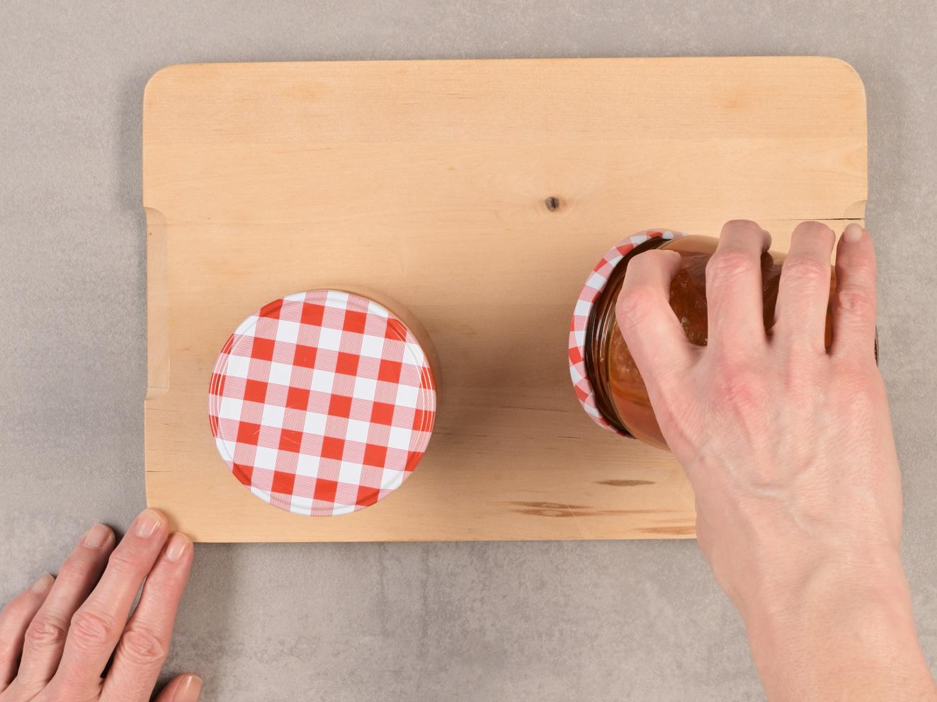 Hände drehen ein Glas Tomatensauce mit kariertem Deckel.