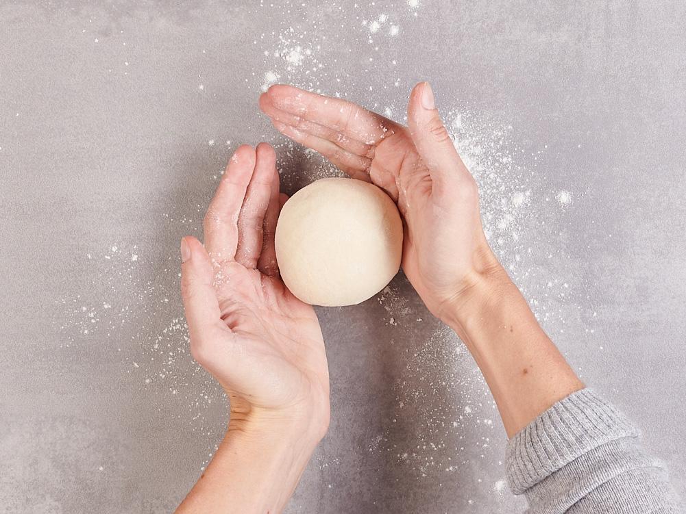 Hände formen einen runden Teigball.
