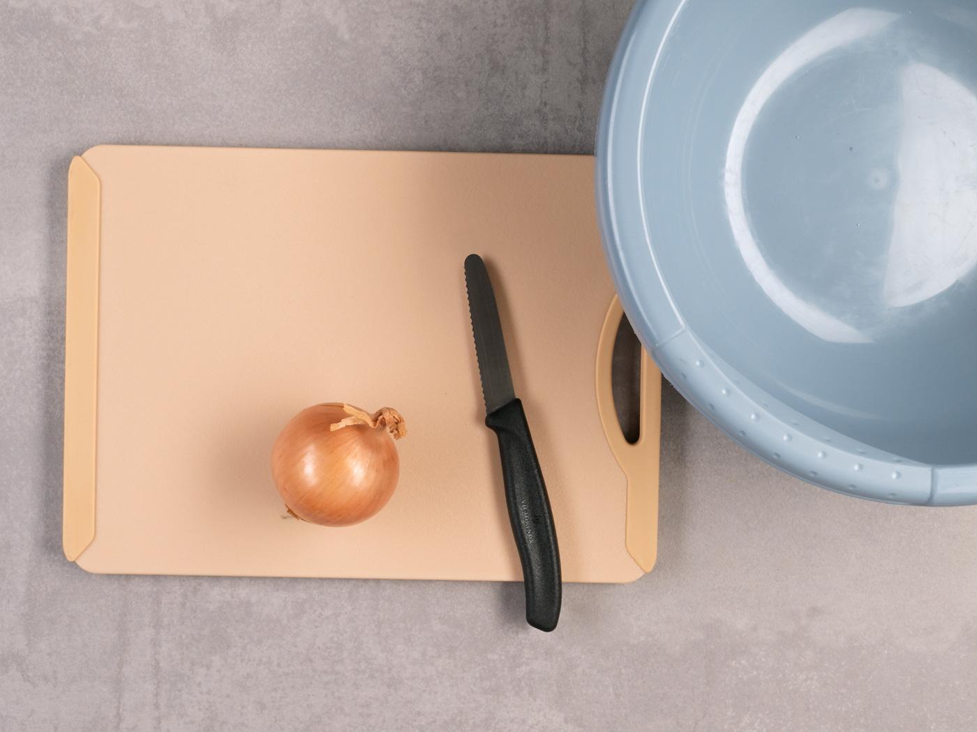 Ganze Zwiebel mit Messer auf Schneidebrett neben einer blauen Schüssel.