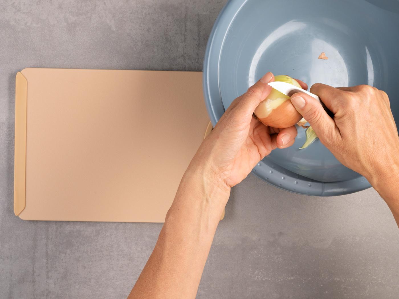 Hände schälen die braune Haut einer Zwiebel über einer Schüssel ab.