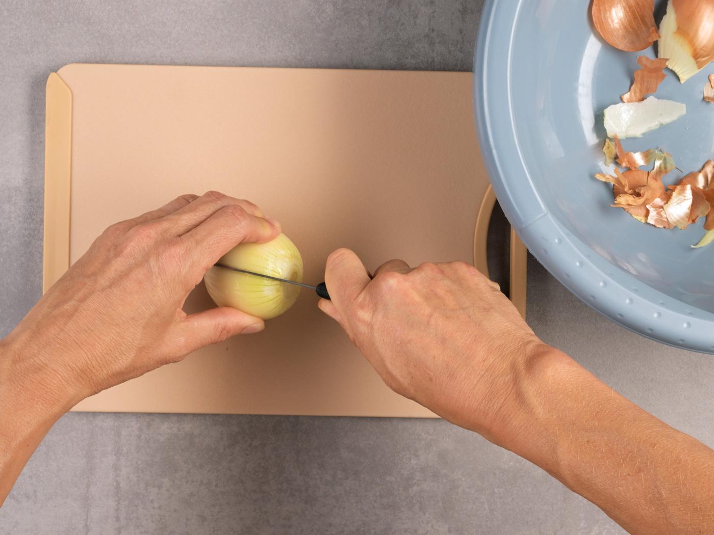 Hände schneiden eine geschälte Zwiebel in zwei Hälften.