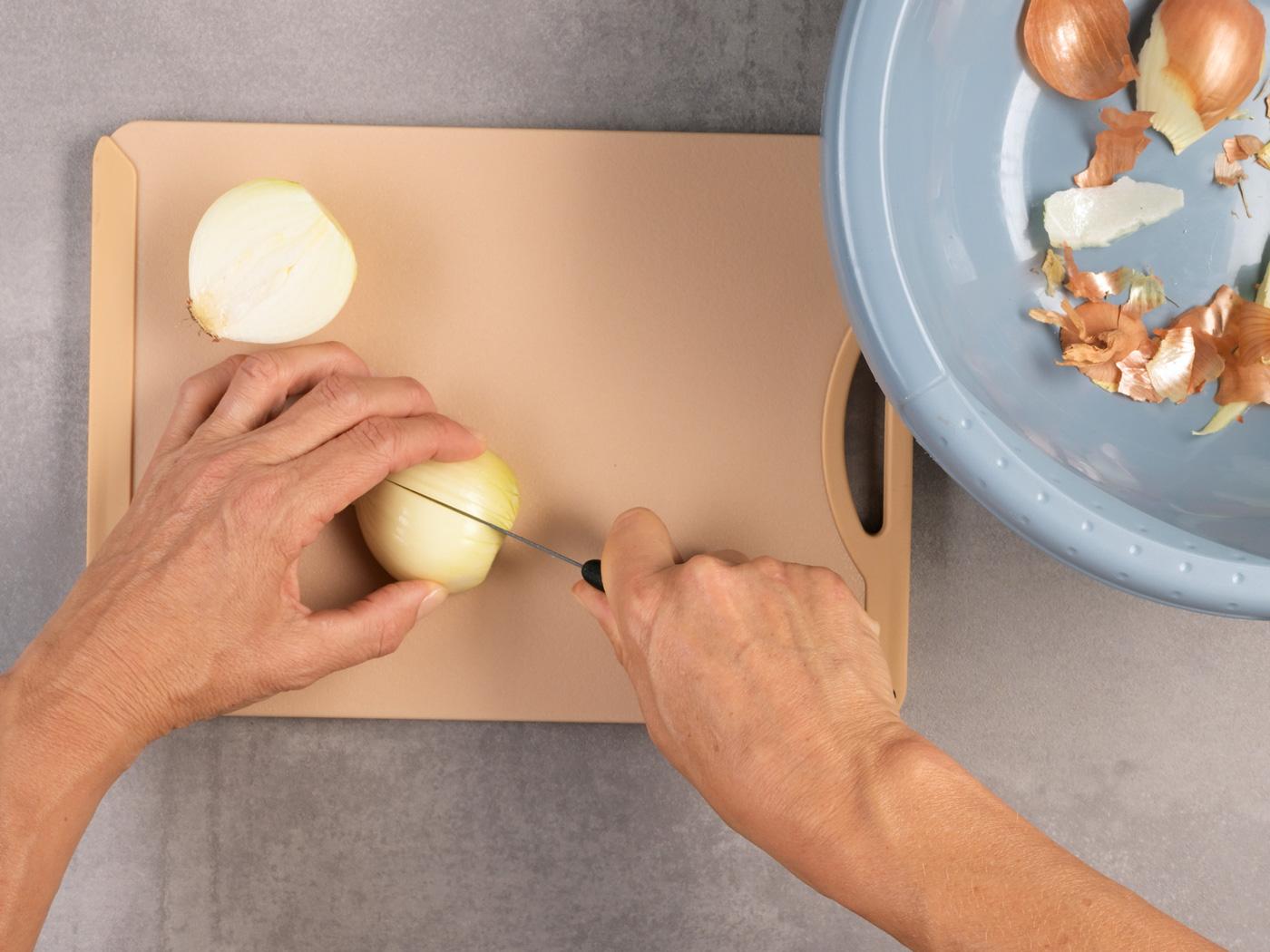 Hände schneiden Zwiebelhälfte auf Brett neben Schüssel mit Schalenresten.