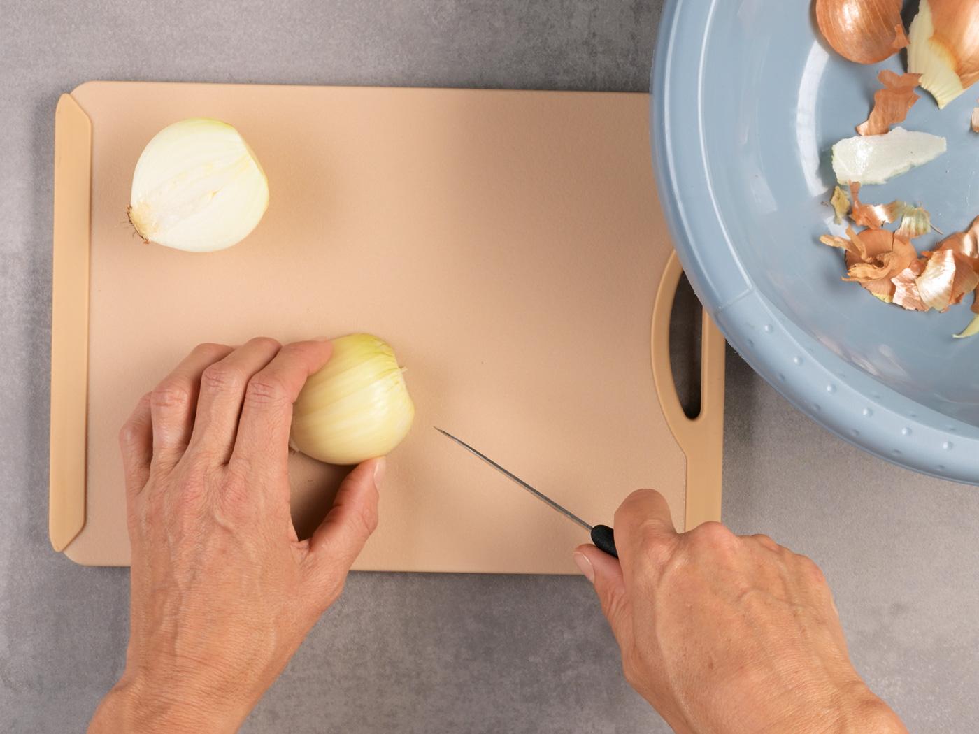 Zwiebelhälfte auf Brett, Messer kurz vor dem nächsten Schnitt.