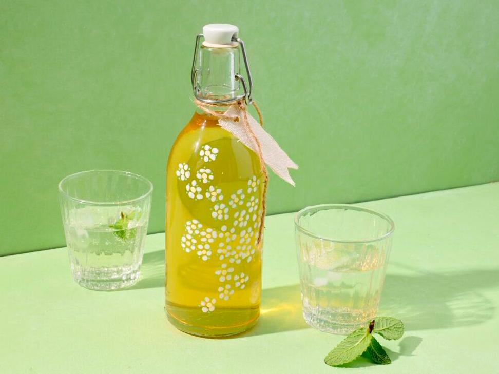 Glasflasche mit hellgelbem Getränk und Schleife, daneben zwei Gläser mit Minze.