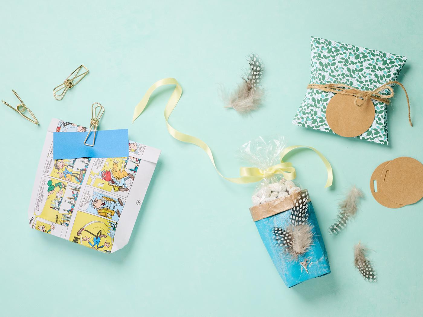 Bunte Geschenkverpackungen aus Papier, Karton und Federn auf hellem Hintergrund.